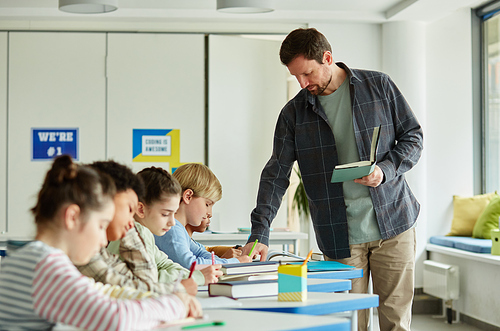 Side view portrait of male teacher helping children taking test in school classroom