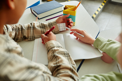 Close up of two children cheating during math test and hiding note in sleeve, copy space