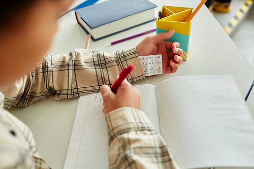 Close up of unrecognizable young boy cheating during test in school and hiding note in sleeve, copy space