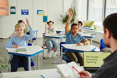 Diverse group of children raising hands in class and answering questions on spelling