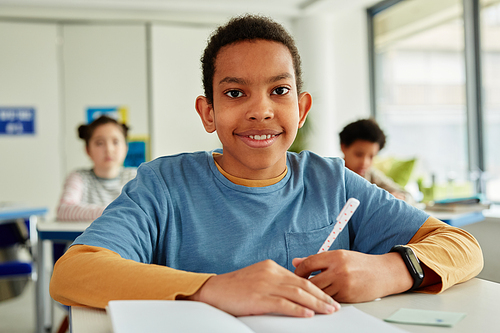 front view portrait of African American schoolboy looking at camera while sitting at desk in school classroom