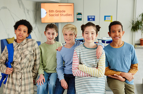 Portrait of diverse group of children looking at camera and smiling while standing together in school classroom