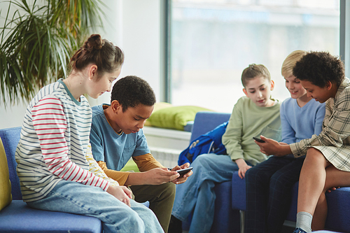 Diverse group of children using smartphones in school during break all dressed in colorful clothes