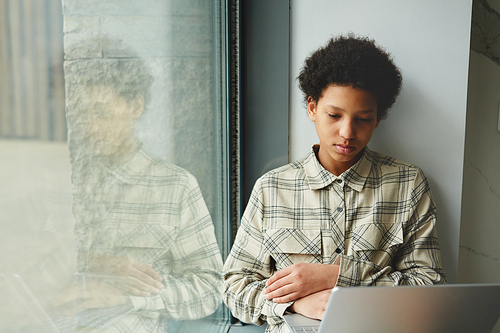 Minimal portrait of young black girl using laptop while sitting by window in school, copy space