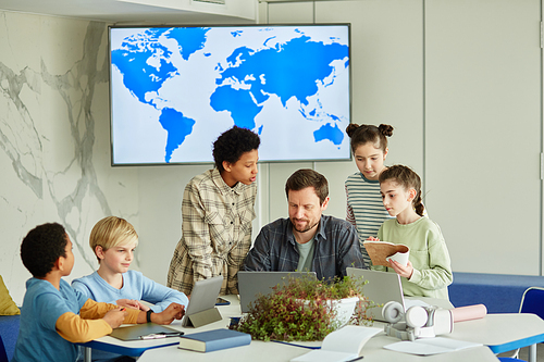 Diverse group of children with male teacher in modern school class on geography with map in background, copy space