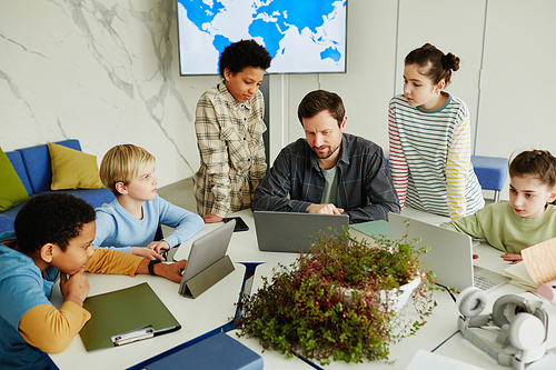 High angle view at diverse group of children with male teacher using laptops in modern school classroom