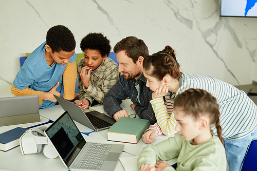 High angle portrait of smiling male teacher with diverse group of children using laptop together in school classroom