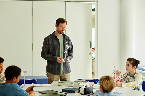 Portrait of bearded male teacher demonstrating project to kids in robotics class, copy space