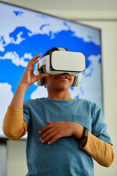 Vertical portrait of young black boy using VR in school classroom with geography map in background