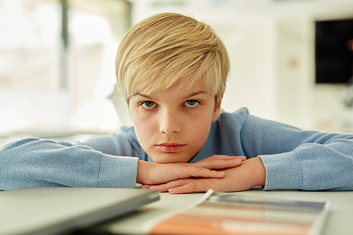 Minimal portrait of bored schoolboy lying on desk in school classroom and looking away