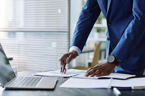 Close up of successful black businessman wearing suit marking data report with pen, copy space