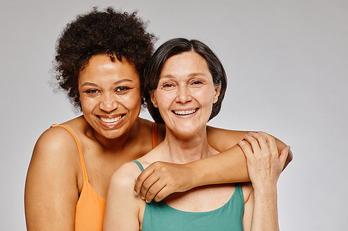 Minimal waist up portrait of two real women embracing and smiling happily against grey background