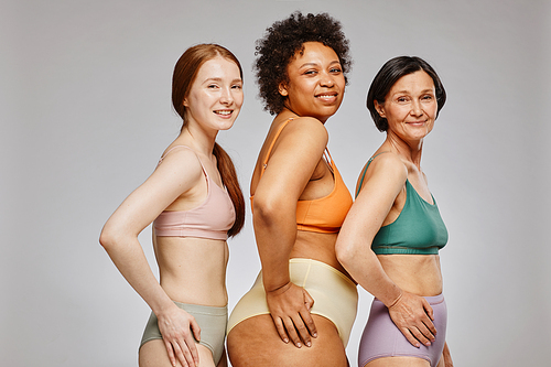 Diverse group of real women wearing underwear and smiling happily against grey background