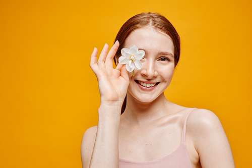 Minima portrait of young red haired woman with flower smiling at camera against vibrant yellow background, copy space