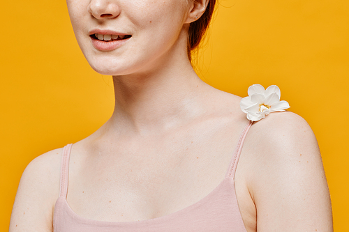 Minimal close up of delicate young woman with flower on fair skin against vibrant yellow background