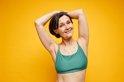 Waist up portrait of carefree adult woman with flowers on skin wearing underwear against vibrant yellow background, copy space