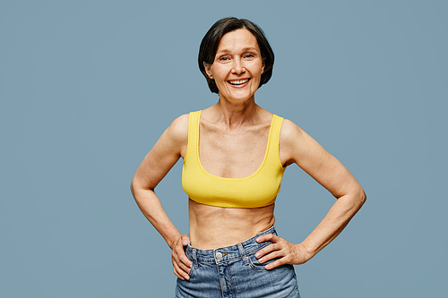 Candid waist up portrait of mature woman smiling at camera while posing against pastel blue background, copy space