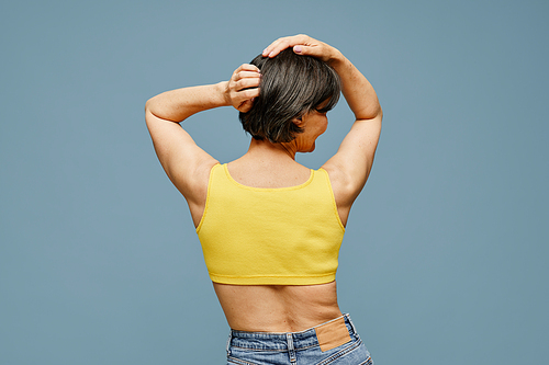 Back view portrait of carefree mature woman posing against pastel blue background, copy space