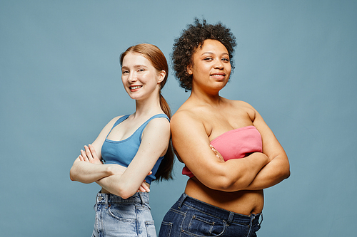 Candid waist up portrait of two confident young women standing against pastel blue background and smiling