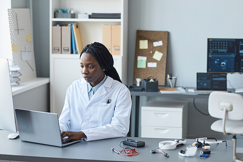 Portrait of young African American woman working in engineering lab and using laptop, copy space
