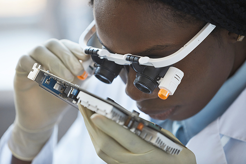 Close up of black young woman inspecting hardware part with magnifying glasses in engineering laboratory