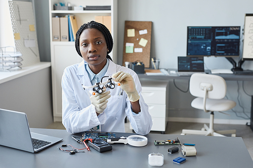 Portrait of young female scientist looking at camera while sitting at workplace in engineering lab, copy space