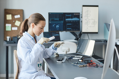 Side view portrait of young female scientist inspecting hardware with magnifying glass in engineering laboratory, copy space