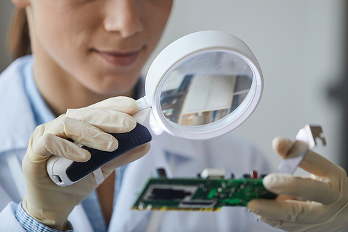 Close up of young woman holding magnifying glass in engineering laboratory, copy space