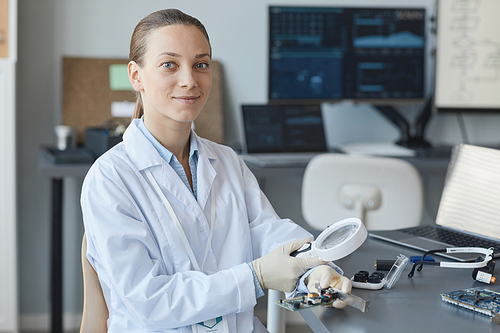 Portrait of young female scientist smiling at camera while sitting at workplace in engineering lab, copy space