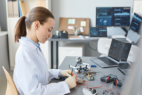 Side view portrait of female lab technician checking hardware parts at quality control station, copy space