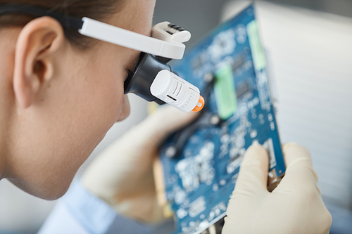 Close up of young woman wearing magnifying visor inspecting computer parts in engineering lab, copy space