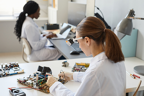 Back view portrait of female engineer working with hardware parts in laboratory, copy space