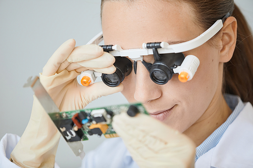 Close up of female engineer wearing magnifiers inspecting electronic parts in laboratory, copy space