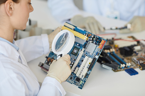 Close up of female lab technician inspecting electronic parts with magnifying glass at quality control, copy space