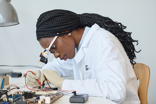 Side view portrait of black female engineer inspecting electronic parts in laboratory, minimal