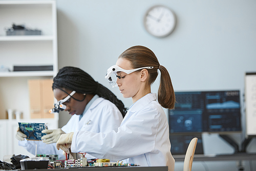 Side view portrait of two female engineers working with electronic parts in laboratory, copy space
