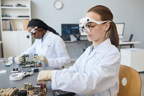 Portrait of two young female engineers working with electronic parts in laboratory, copy space