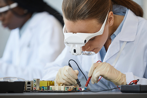 Close up portrait of young female engineer inspecting computer parts with magnifiers at quality control line