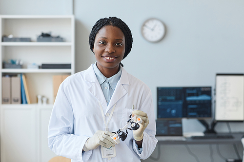Waist up portrait of young black woman as female engineer smiling at camera in laboratory, copy space
