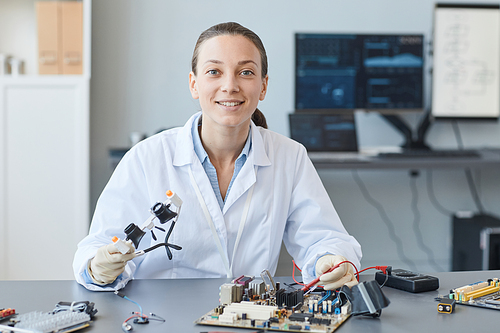 Portrait of smiling young woman as female engineer looking at camera while working in lab, copy space
