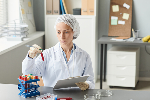 Portrait of female lab technician mixing liquid in test tube while working with blood analysis in laboratory, copy space