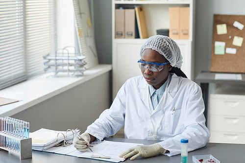 Portrait of black female scientist filling in charts while working in medical laboratory, copy space