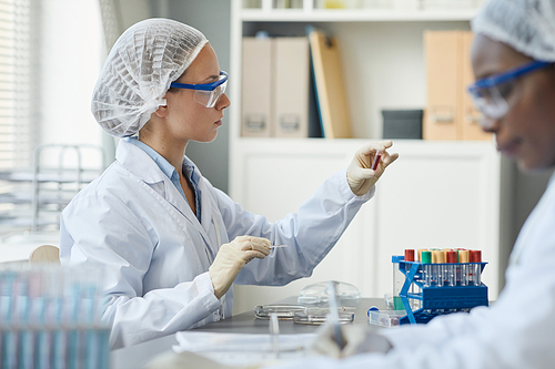 Side view portrait of young woman holding test tube in laboratory while doing medical research