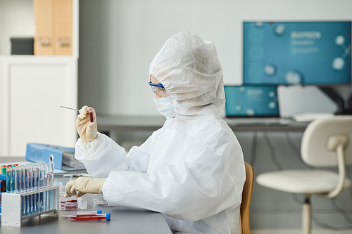Portrait of woman wearing full protective gear while holding petri dish in medical laboratory, copy space