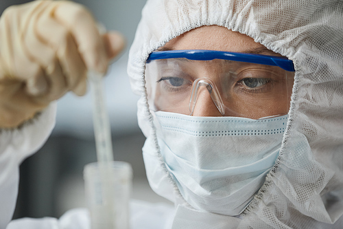 Side view portrait of two female scientists wearing full protective gear while performing research with hazardous materials in medical laboratory