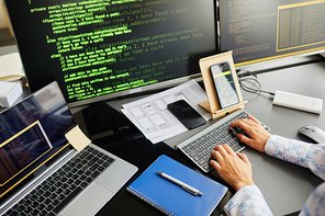 Close-up of IT worker developing new software on computer typing on keyboard and connecting smartphone and laptop with codes at her workplace