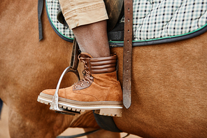 Side view closeup of leather boot in stirrups with unrecognizable woman riding horse in ranch, copy space