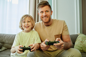 Front view portrait of father and son playing video games together and smiling happily