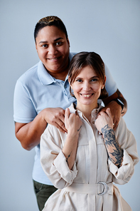 Vertical portrait of happy gay couple smiling at camera against light blue background