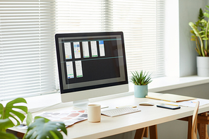 Minimal background image of computer with mobile app designs on screen at workplace table